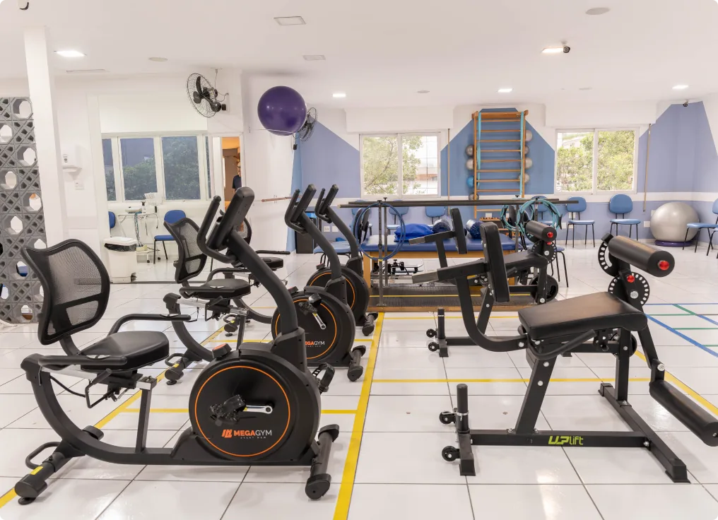 Sala de exercícios com bicicletas ergométricas, aparelhos de fortalecimento e espelhos.