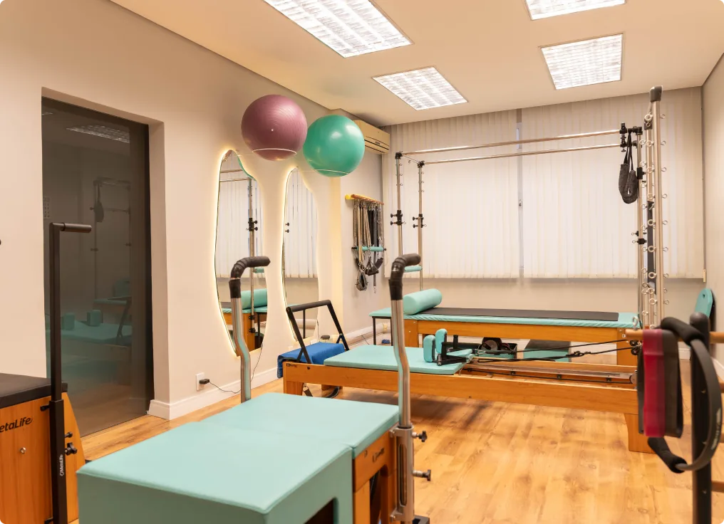 Sala de Pilates com aparelhos, bolas de exercício e piso de madeira.
